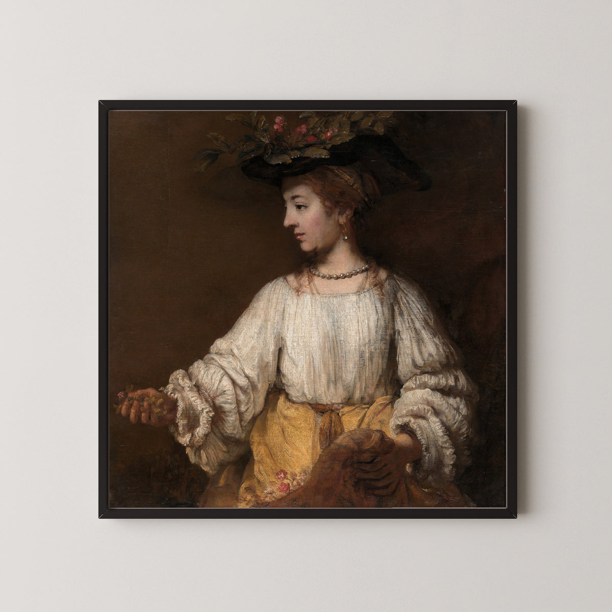 Framed art print of Flora by Rembrandt van Rijn, in a black frame on a pale wall