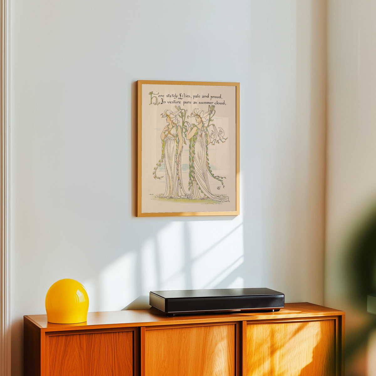 Framed art print of Flora's Feast: Lilies by Walter Crane, in a light wood frame on a white wall above an orange sideboard