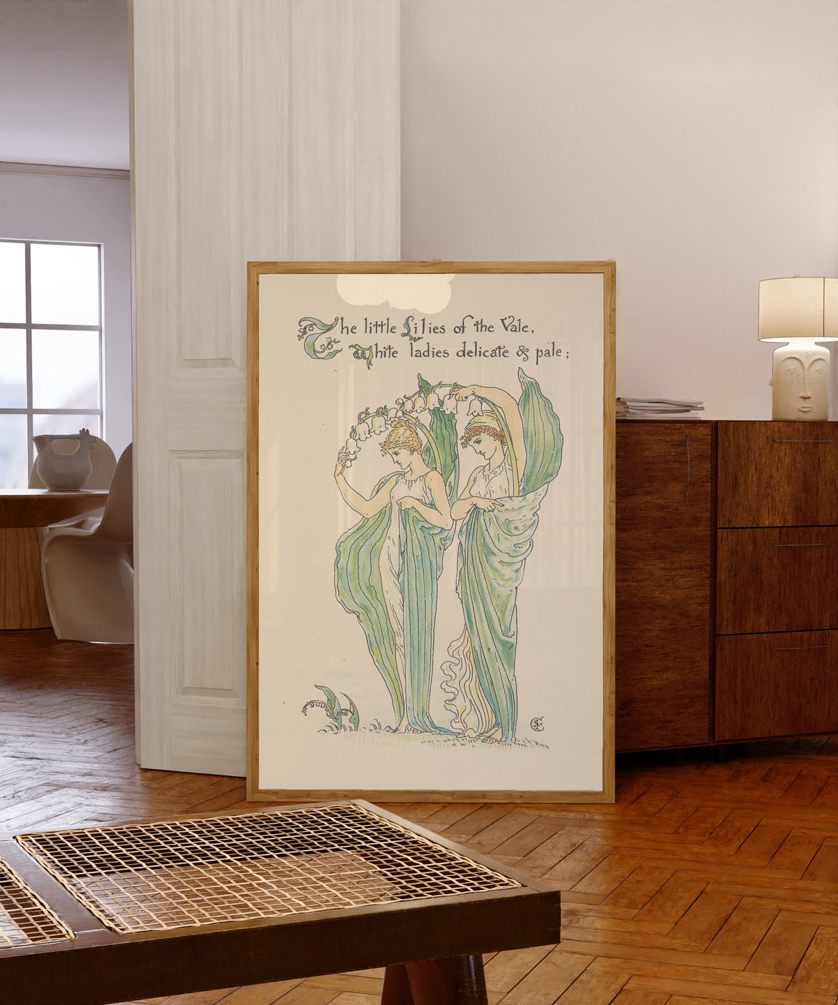 Framed art print of Flora's Feast: Lilies of the Vale by Walter Crane, in a light wood frame leaning in a warm room with a parquet floor