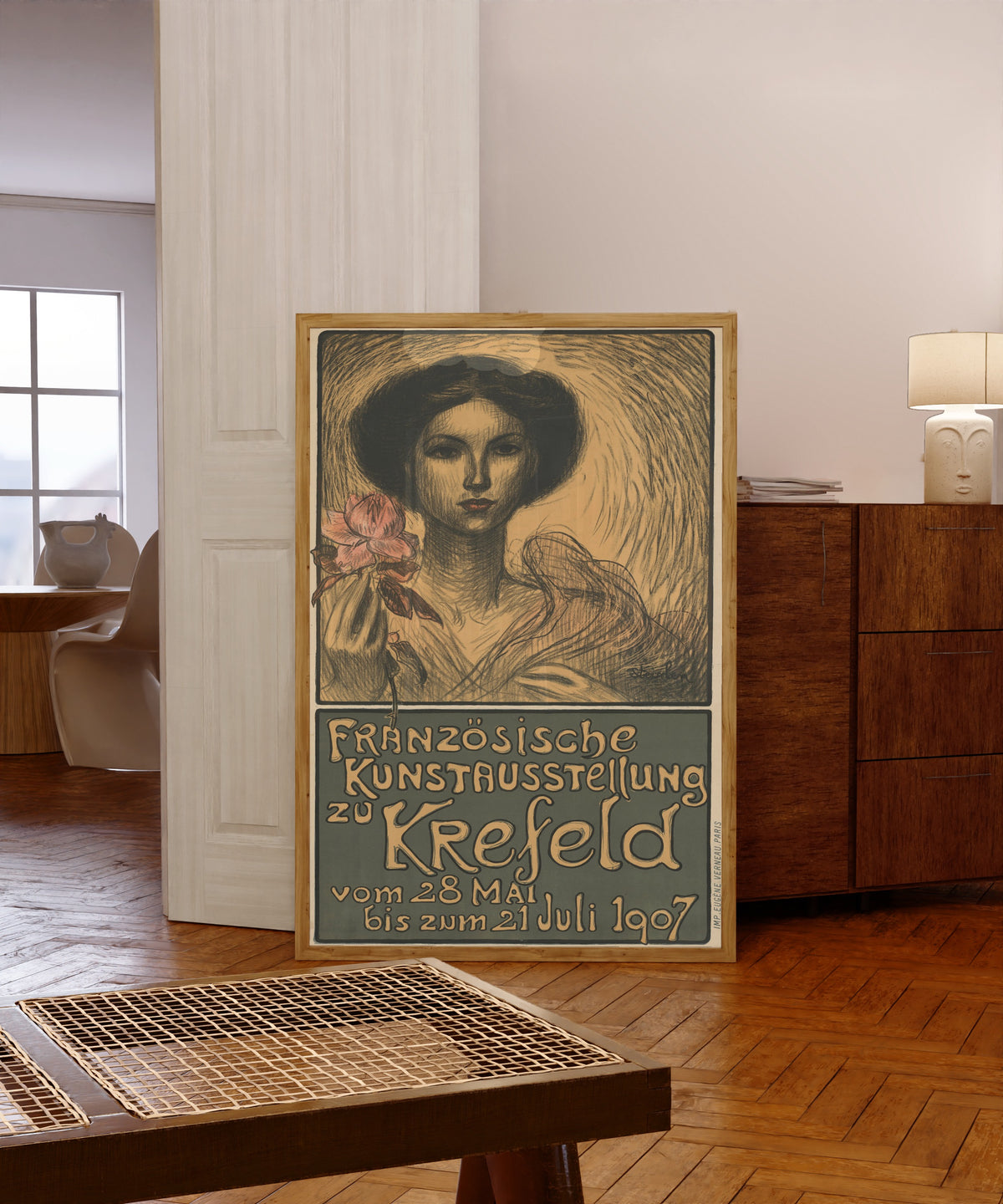 Framed art print of Französische Kunstausstellung zu Krefeld by Théophile Steinlen, in a light wood frame leaning in a warm room with a parquet floor