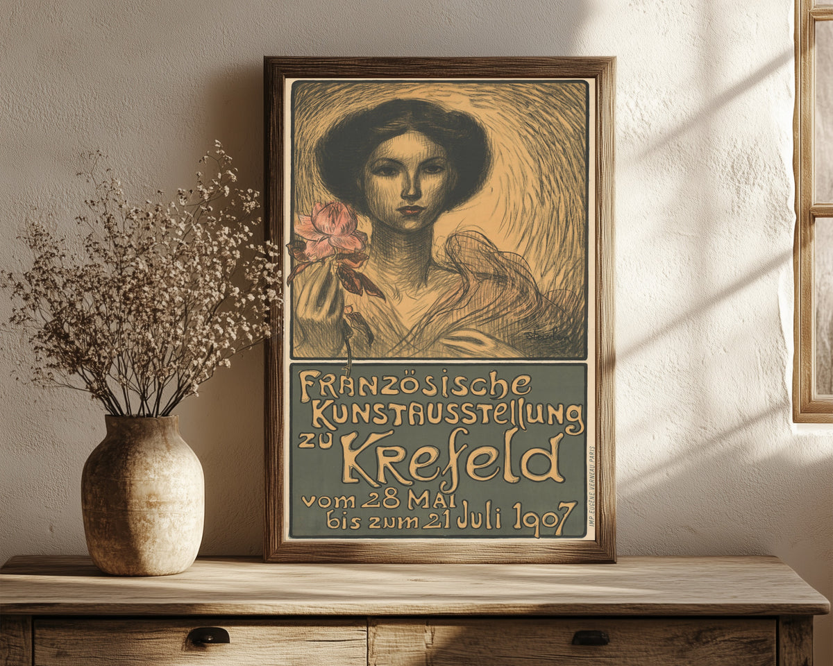 Framed art print of Französische Kunstausstellung zu Krefeld by Théophile Steinlen, in a dark wood frame leaning on a rustic console beside dried flowers