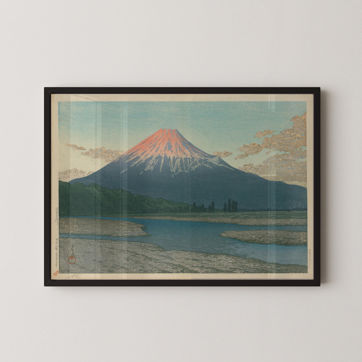 Framed art print of Fuji River by Kawase Hasui, in a black frame on a pale wall