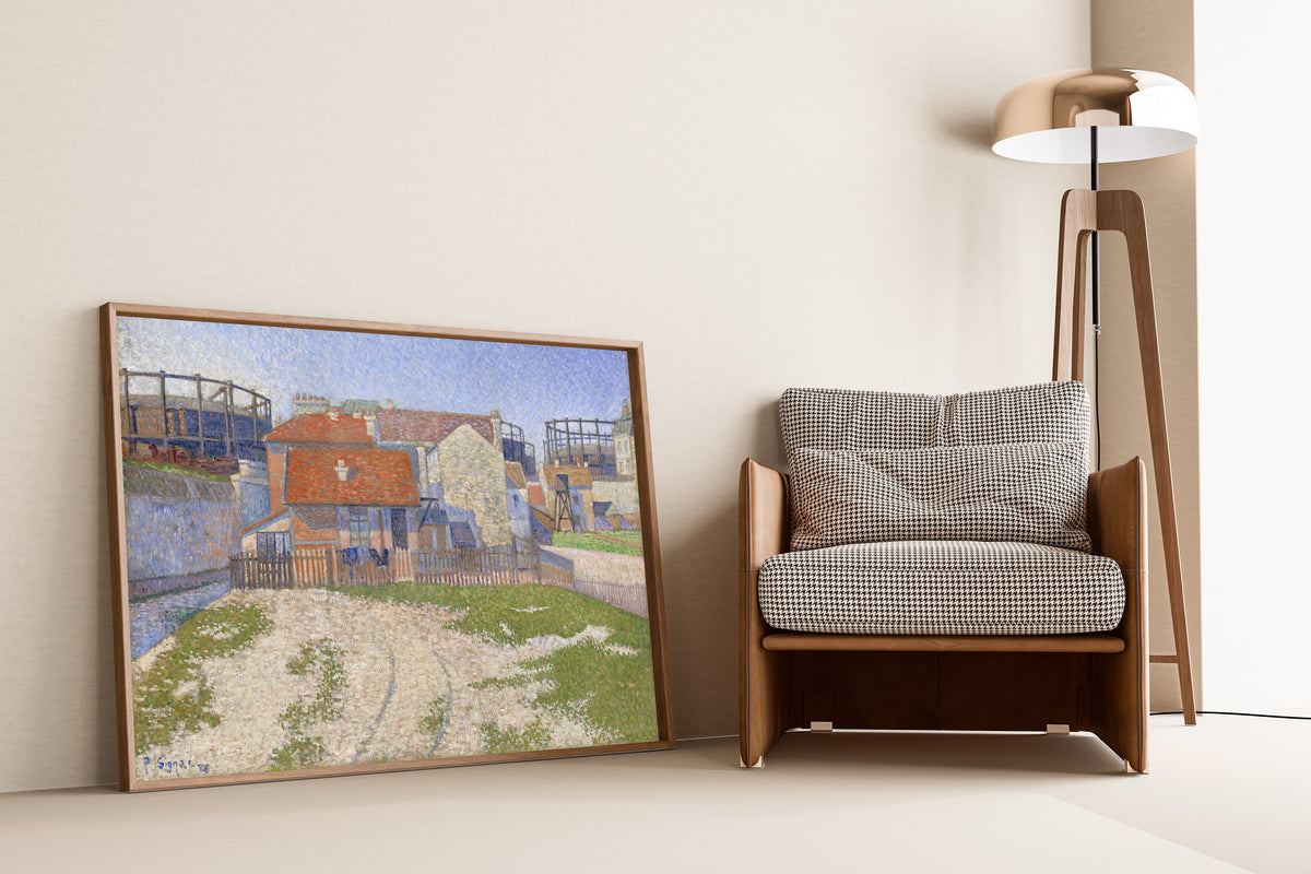 Framed art print of Gasometers at Clichy by Paul Signac, leaning against a wall beside an armchair and a floor lamp
