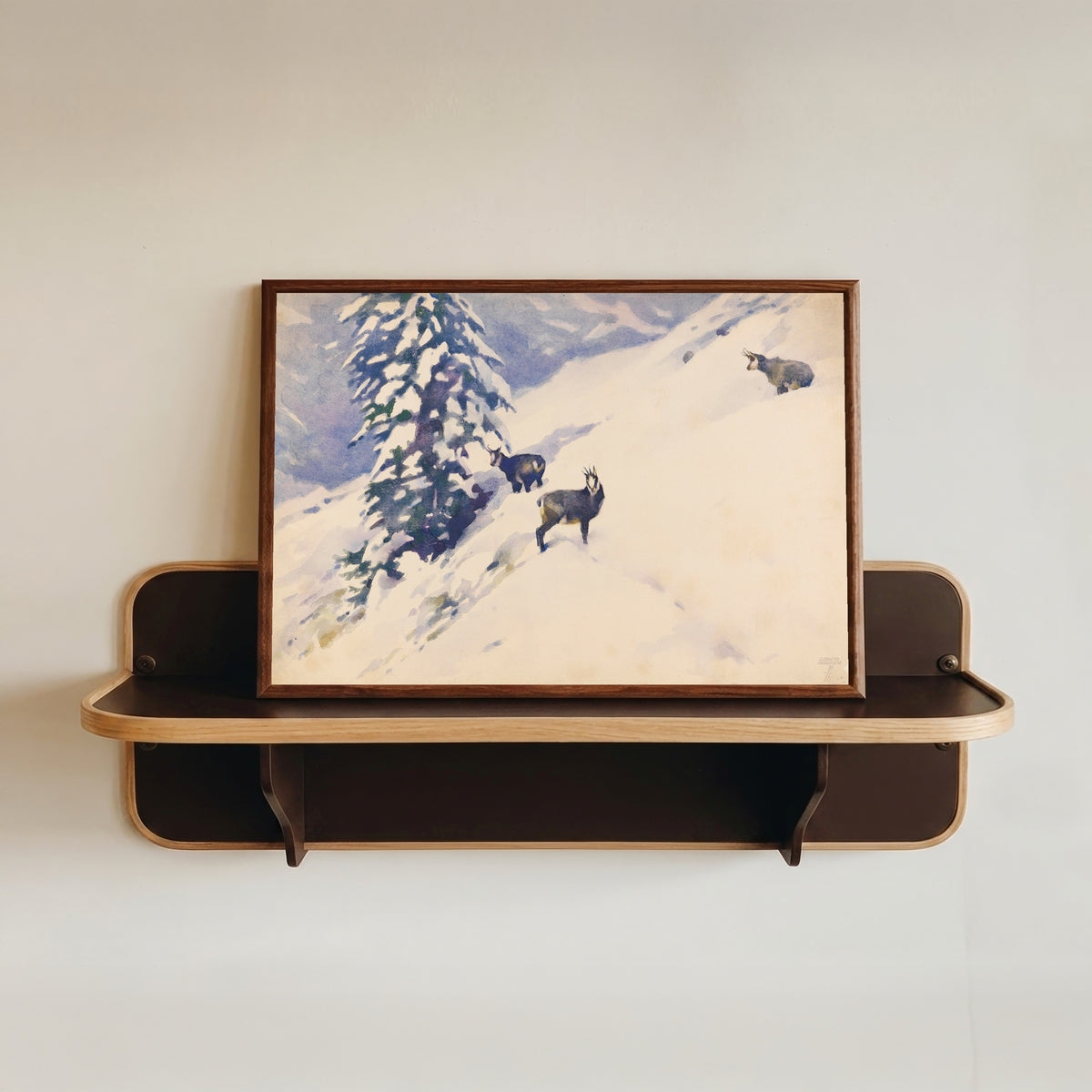 Framed art print of Gemsen im Schnee by Ludwig Hohlwein, in a dark wood frame resting on a wall shelf
