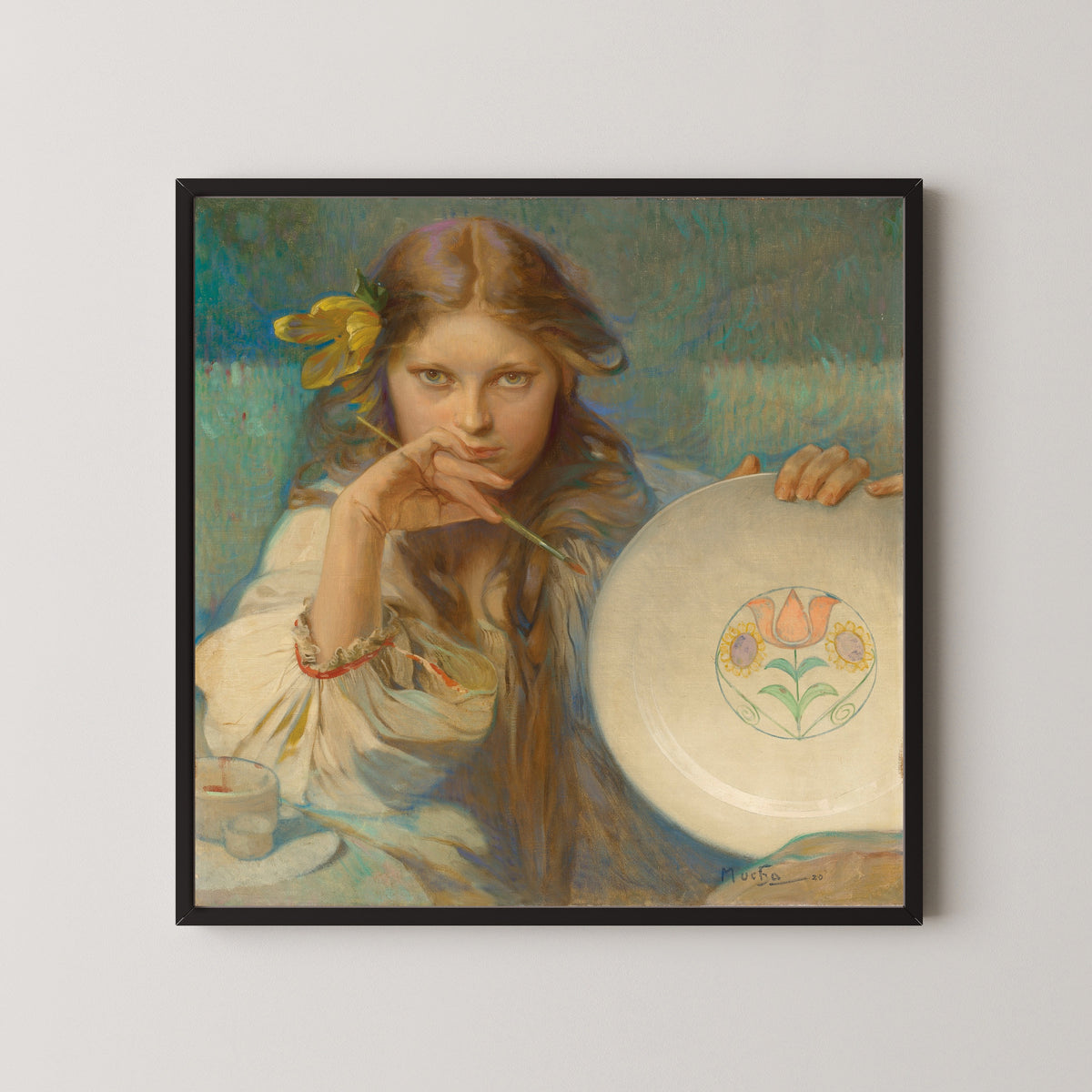 Framed art print of Girl with a Plate with a Folk Motif by Alphonse Mucha, in a black frame on a pale wall