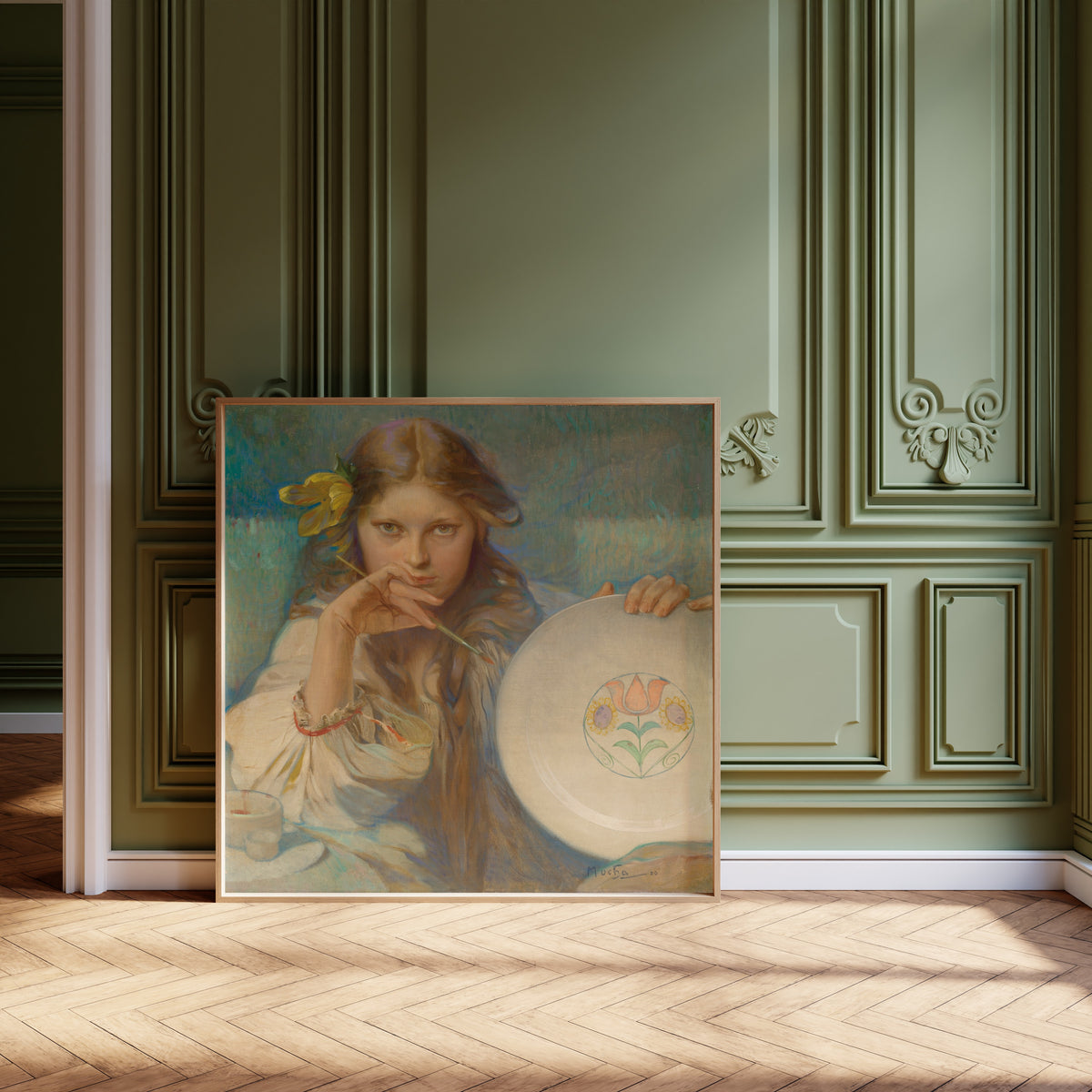 Framed art print of Girl with a Plate with a Folk Motif by Alphonse Mucha, leaning against olive-green panelling on a herringbone floor