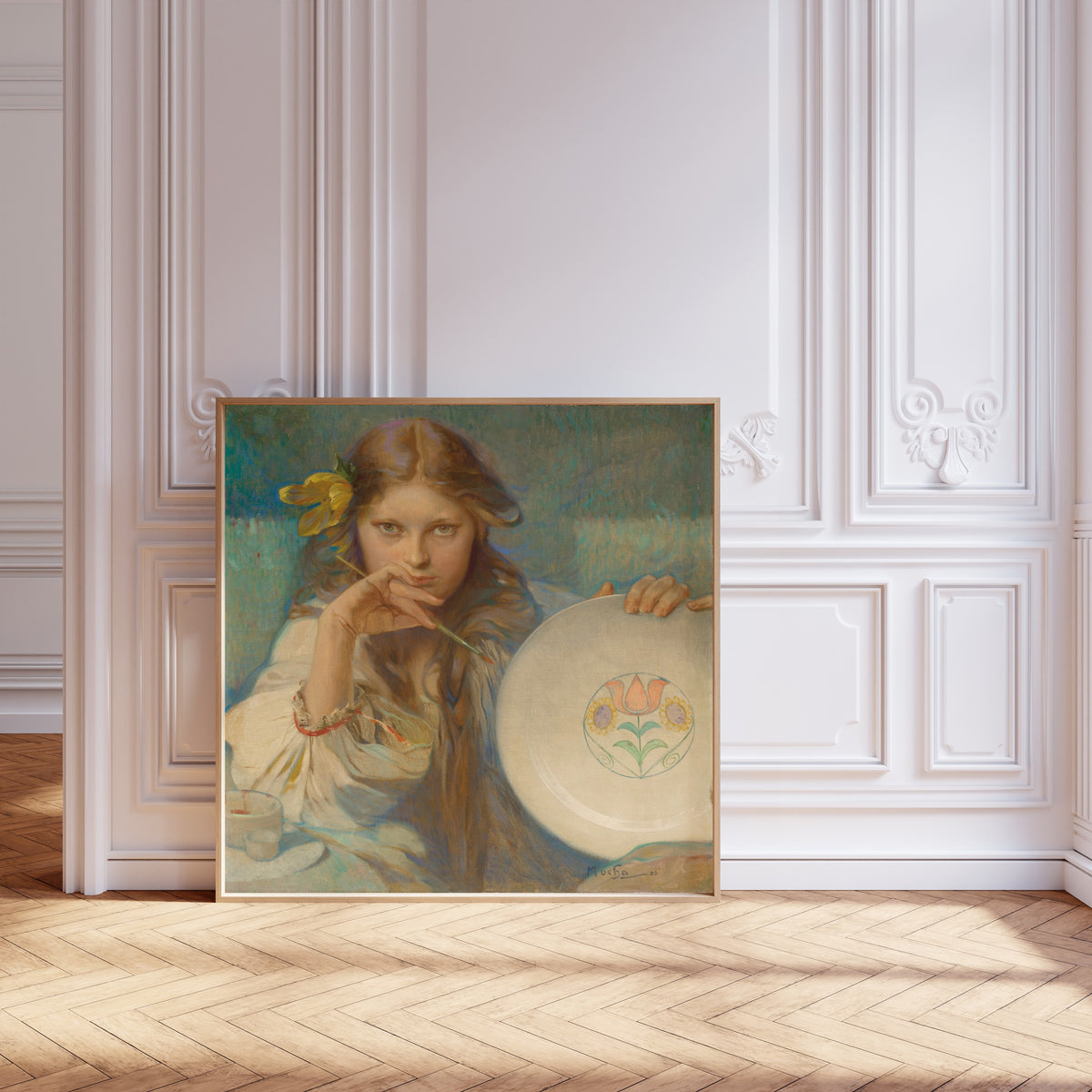 Framed art print of Girl with a Plate with a Folk Motif by Alphonse Mucha, leaning against pale pink panelling on a herringbone floor