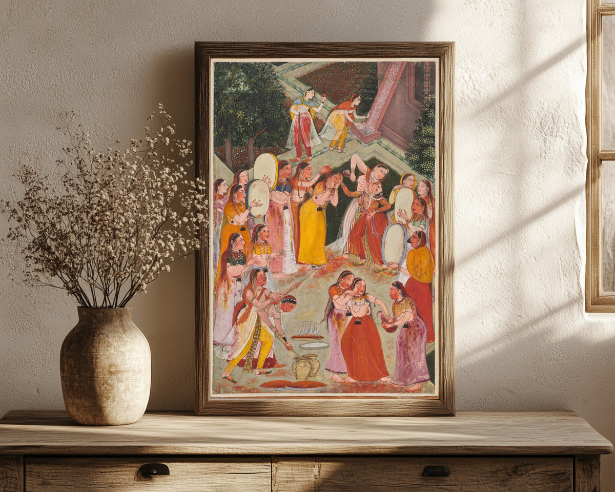 Framed art print of Girls Spraying Each Other at Holi by Bikaner school, in a dark wood frame leaning on a rustic console beside dried flowers