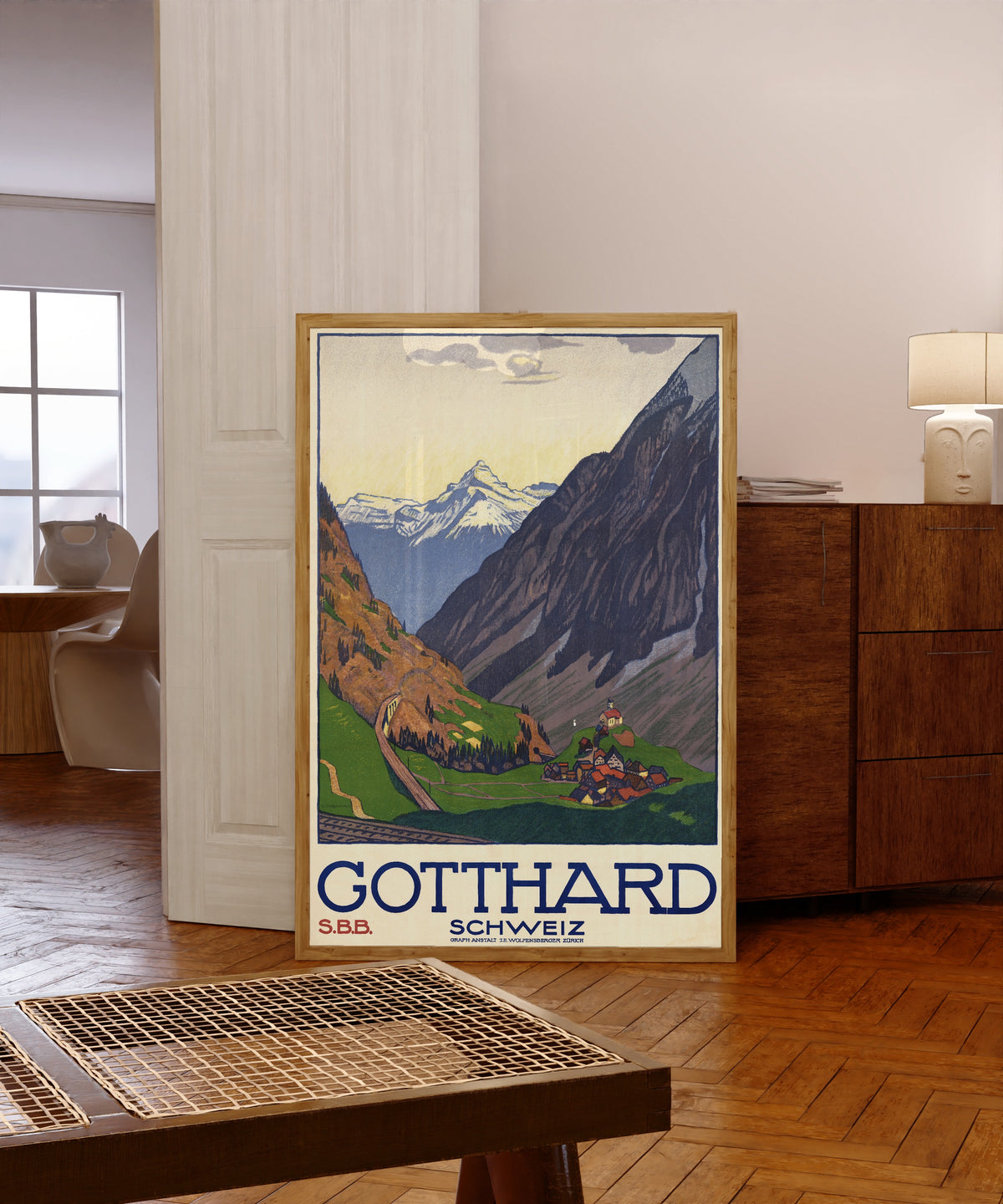 Framed art print of Gotthard Schweiz by Emil Cardinaux, in a light wood frame leaning in a warm room with a parquet floor