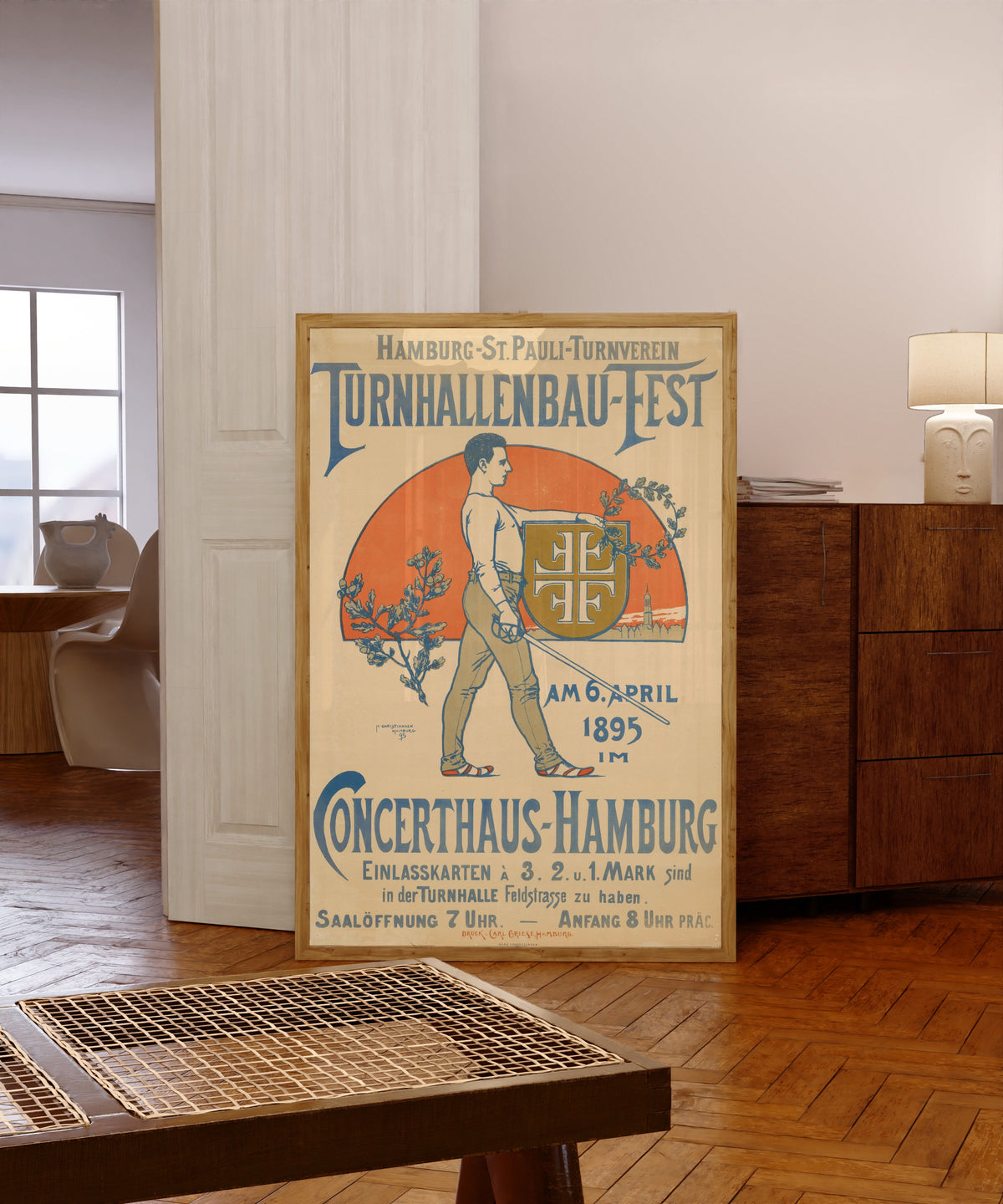 Framed art print of Hamburg-St. Pauli Turnverein: Turnhallenbau-Fest by Hans Christiansen, in a light wood frame leaning in a warm room with a parquet floor