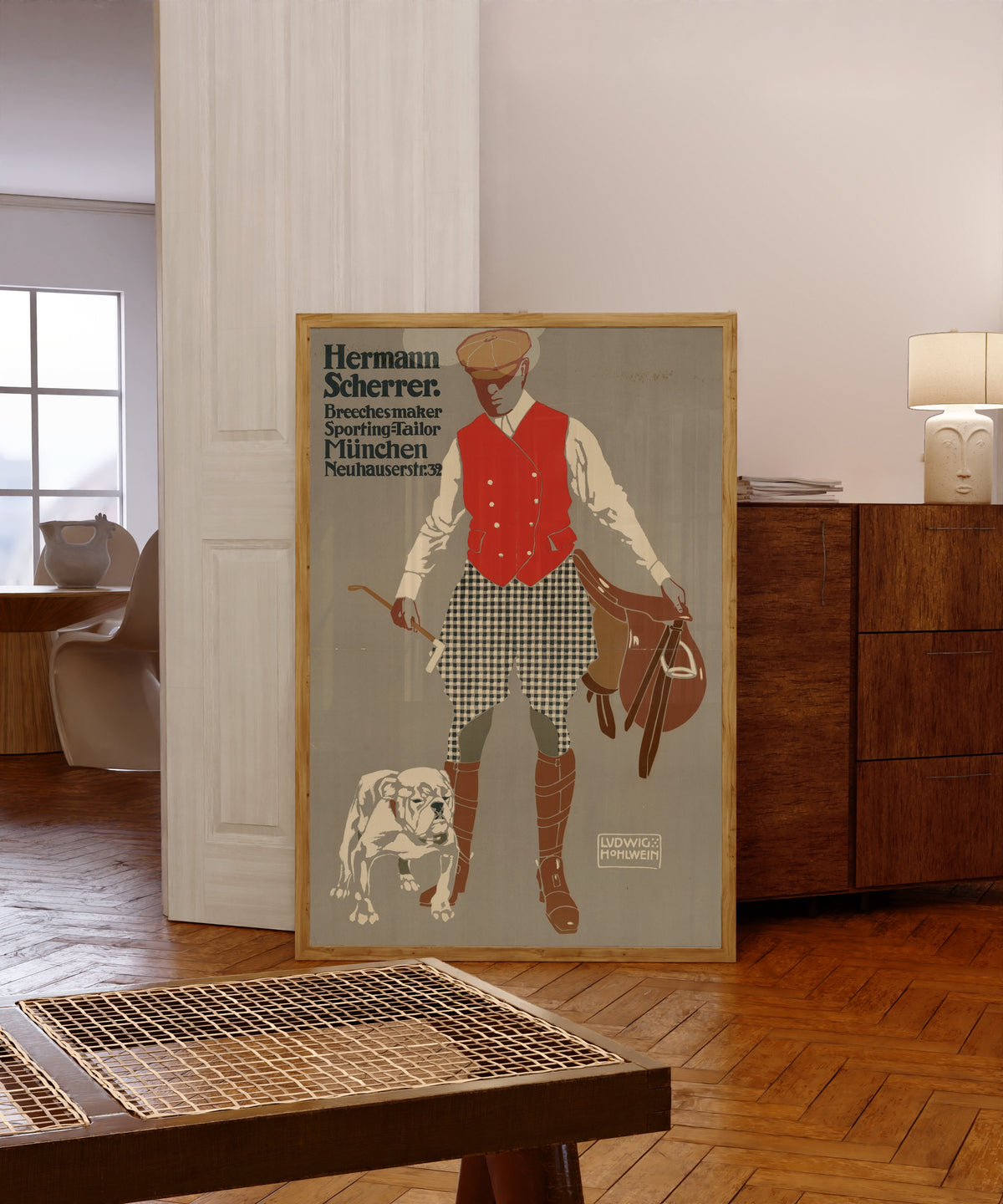 Framed art print of Hermann Scherrer: Breechesmaker, Sporting-Tailor… by Ludwig Hohlwein, in a light wood frame leaning in a warm room with a parquet floor