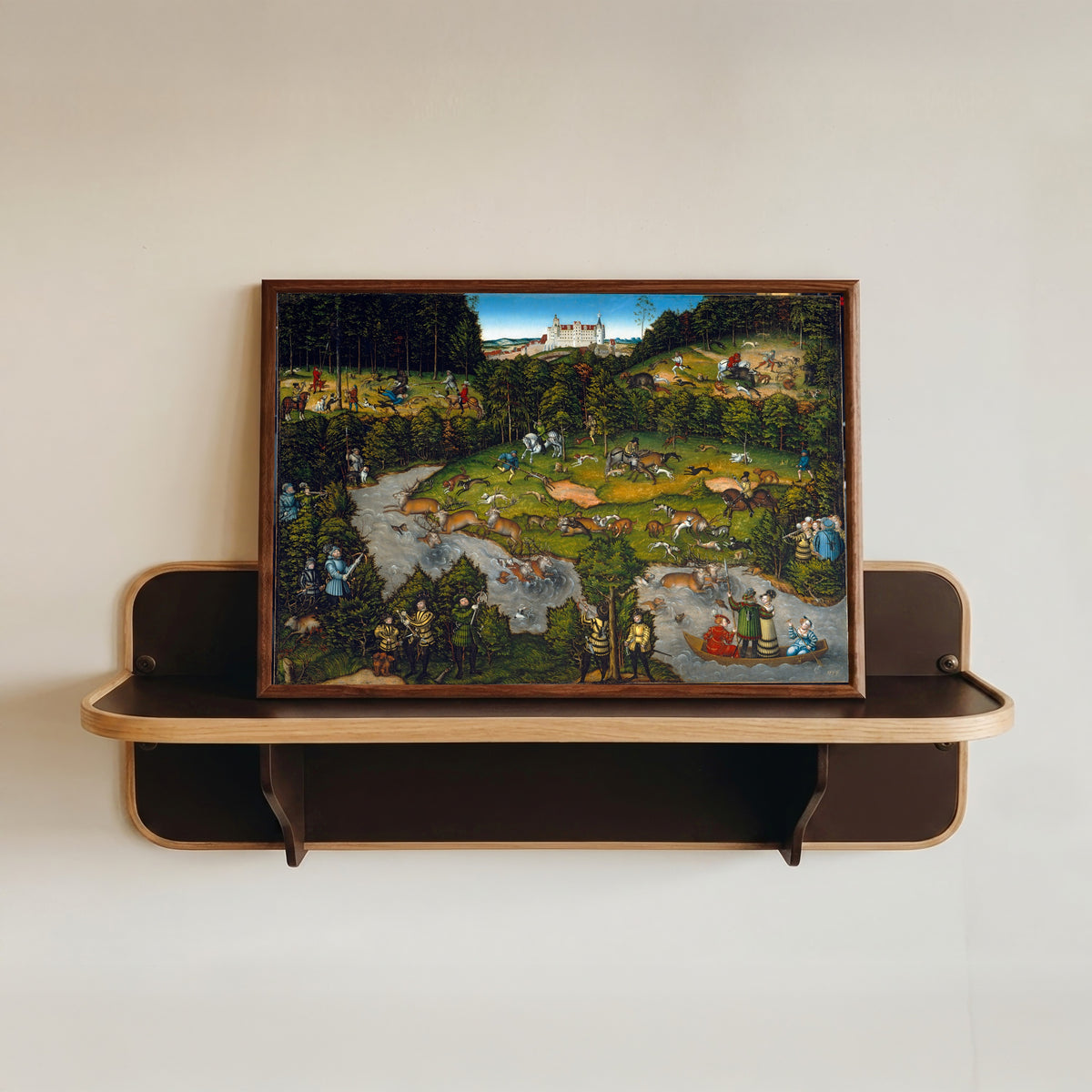 Framed art print of Hunting near Hartenfels Castle by Lucas Cranach the Elder, in a dark wood frame resting on a wall shelf