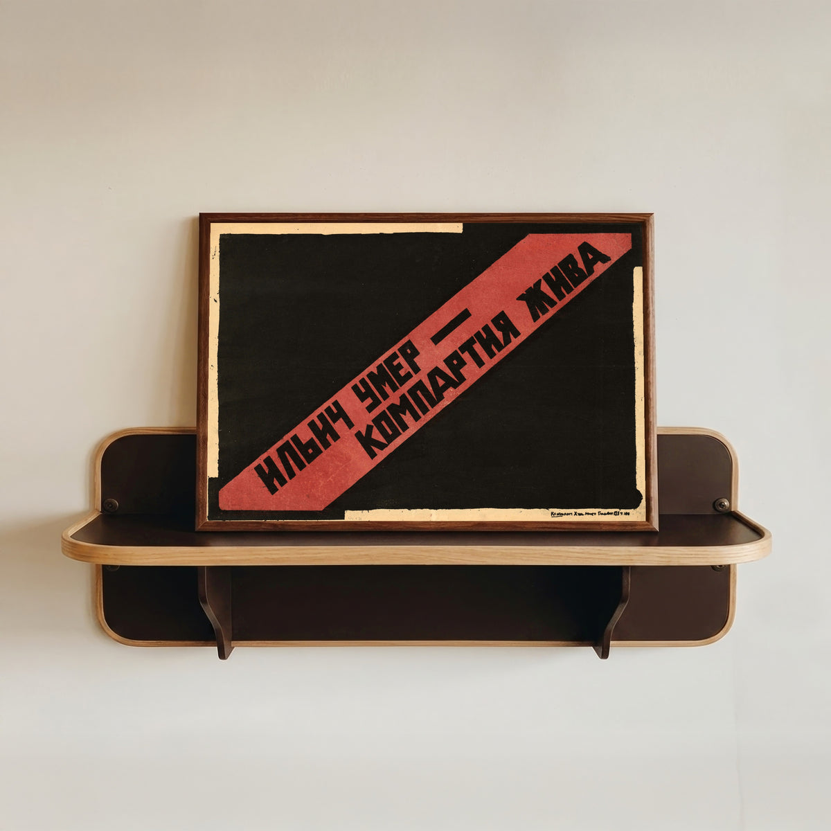 Framed art print of Ilyich is dead, the Communist Party lives, in a dark wood frame resting on a wall shelf
