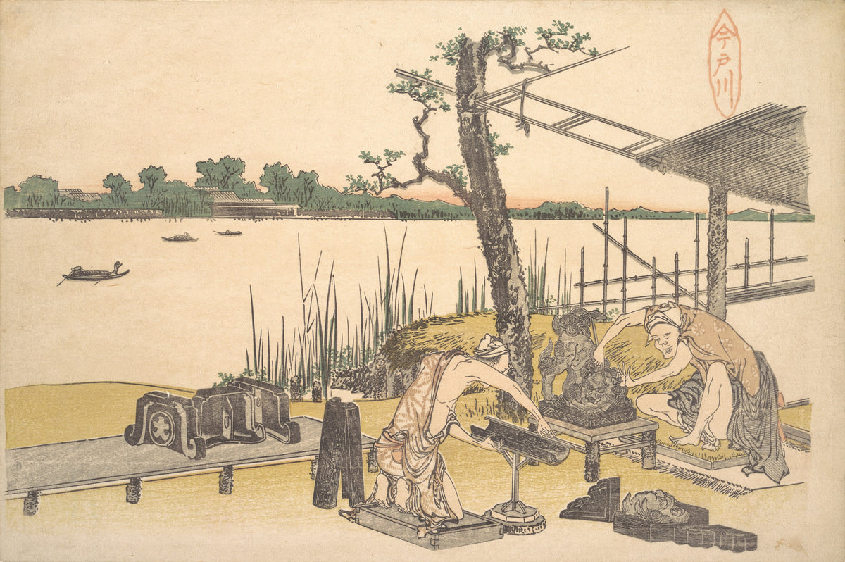 Imadogawa by Katsushika Hokusai — Two workmen handle dark moulded pieces on a riverbank bench