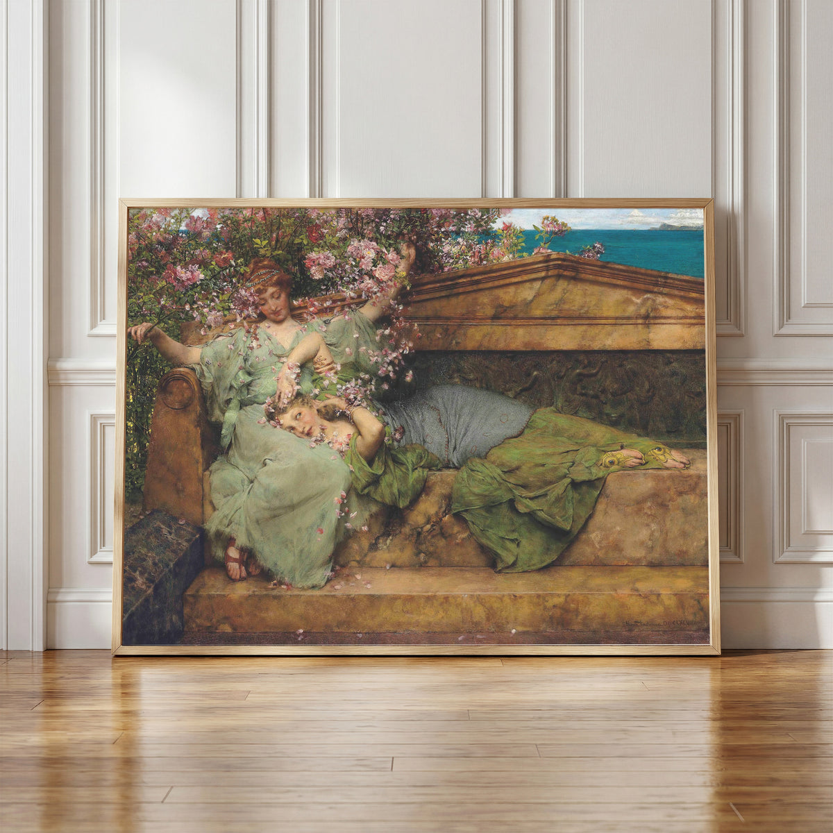 Framed art print of In a Rose Garden by Lawrence Alma-Tadema, in a light wood frame leaning against a panelled white wall