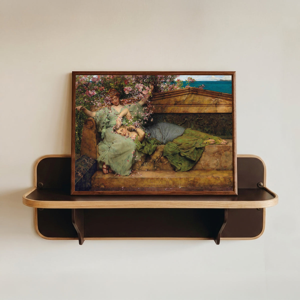 Framed art print of In a Rose Garden by Lawrence Alma-Tadema, in a dark wood frame resting on a wall shelf