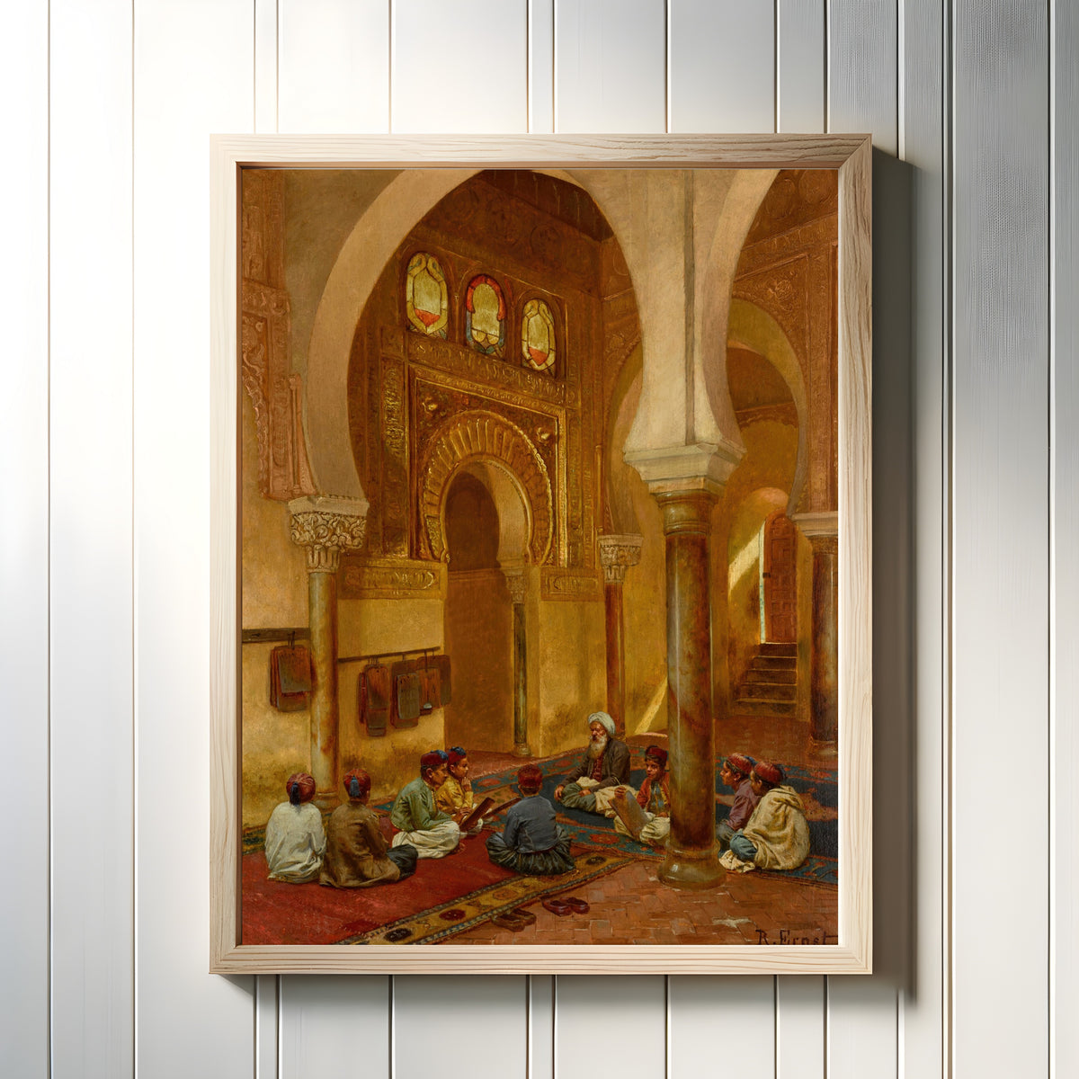 Framed art print of In the Madrasa by Rudolf Ernst, in a light wood frame on a white panelled wall