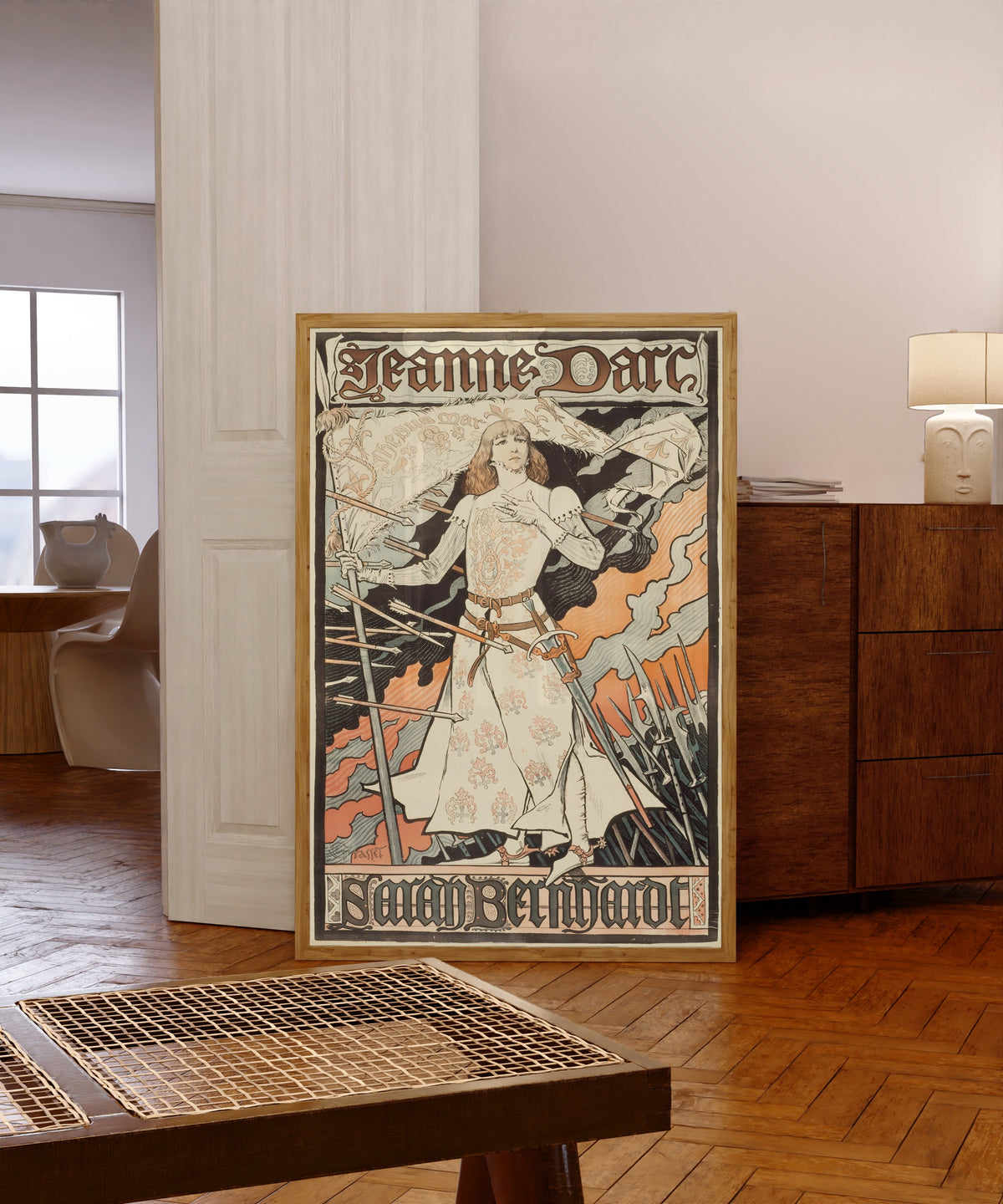 Framed art print of Jeanne d'Arc-Sarah Bernhardt by Eugène Grasset, in a light wood frame leaning in a warm room with a parquet floor