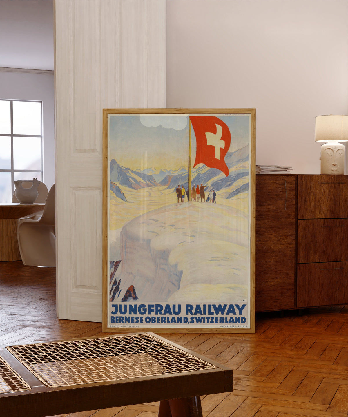 Framed art print of Jungfrau Railway: Bernese Oberland, Switzerland by Emil Cardinaux, in a light wood frame leaning in a warm room with a parquet floor