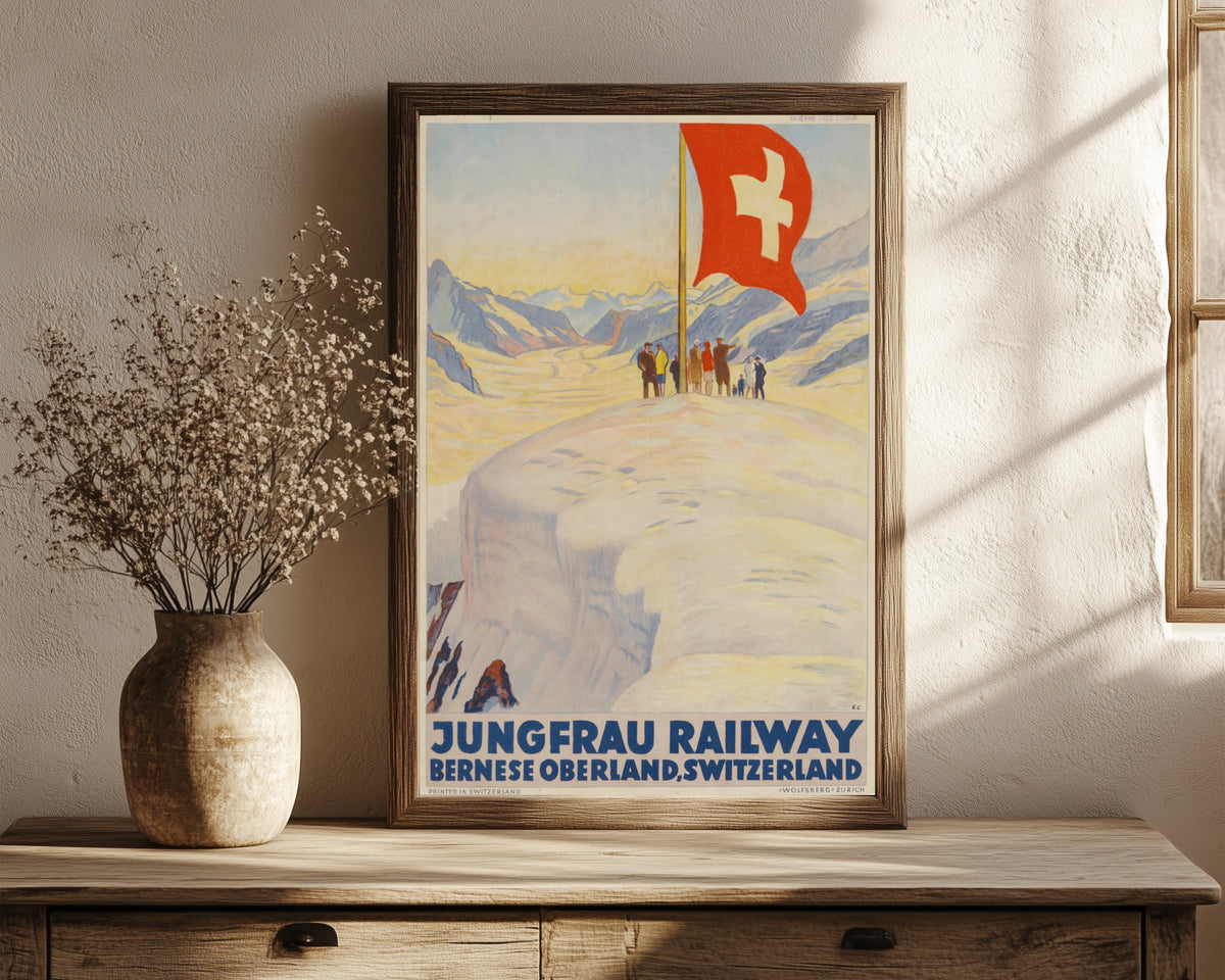 Framed art print of Jungfrau Railway: Bernese Oberland, Switzerland by Emil Cardinaux, in a dark wood frame leaning on a rustic console beside dried flowers