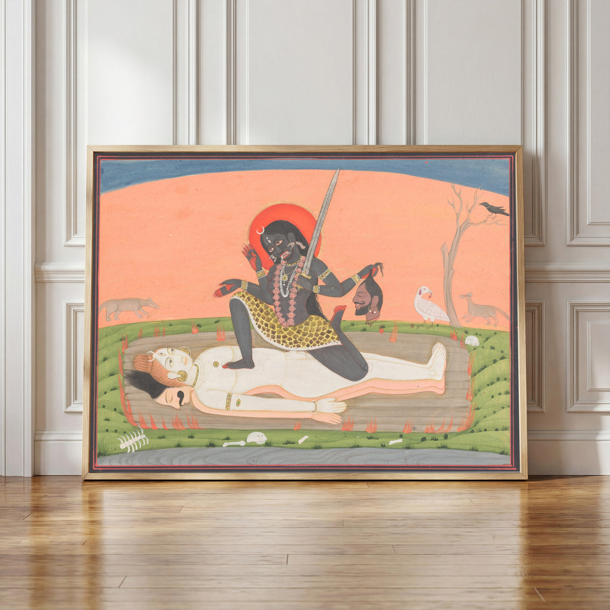Framed art print of Kali on Shiva by Pahari school, in a light wood frame leaning against a panelled white wall