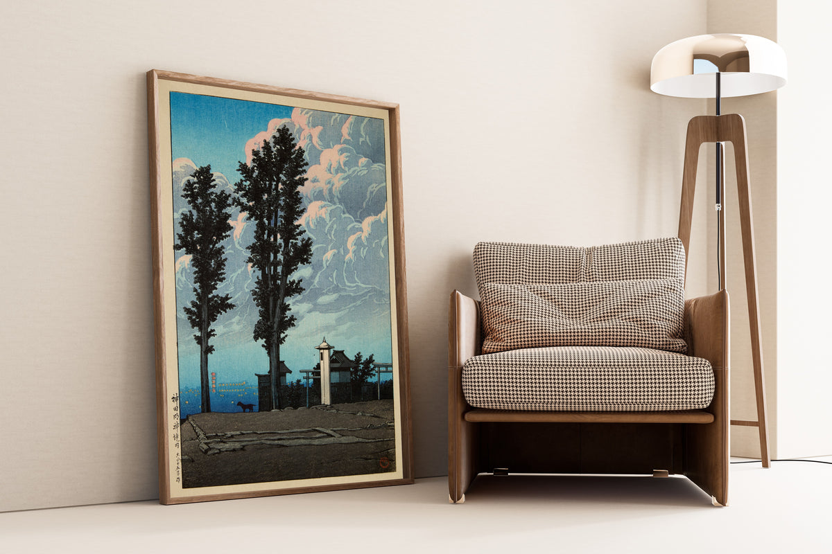 Framed art print of Kanda Myojin Shrine Precinct by Kawase Hasui, leaning against a wall beside an armchair and a floor lamp