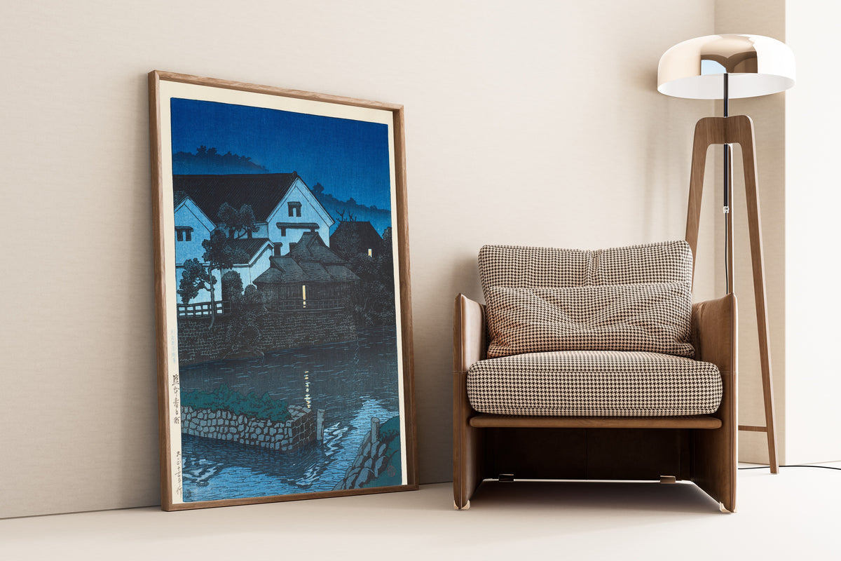 Framed art print of Kasuga-cho, Kumamoto by Kawase Hasui, leaning against a wall beside an armchair and a floor lamp