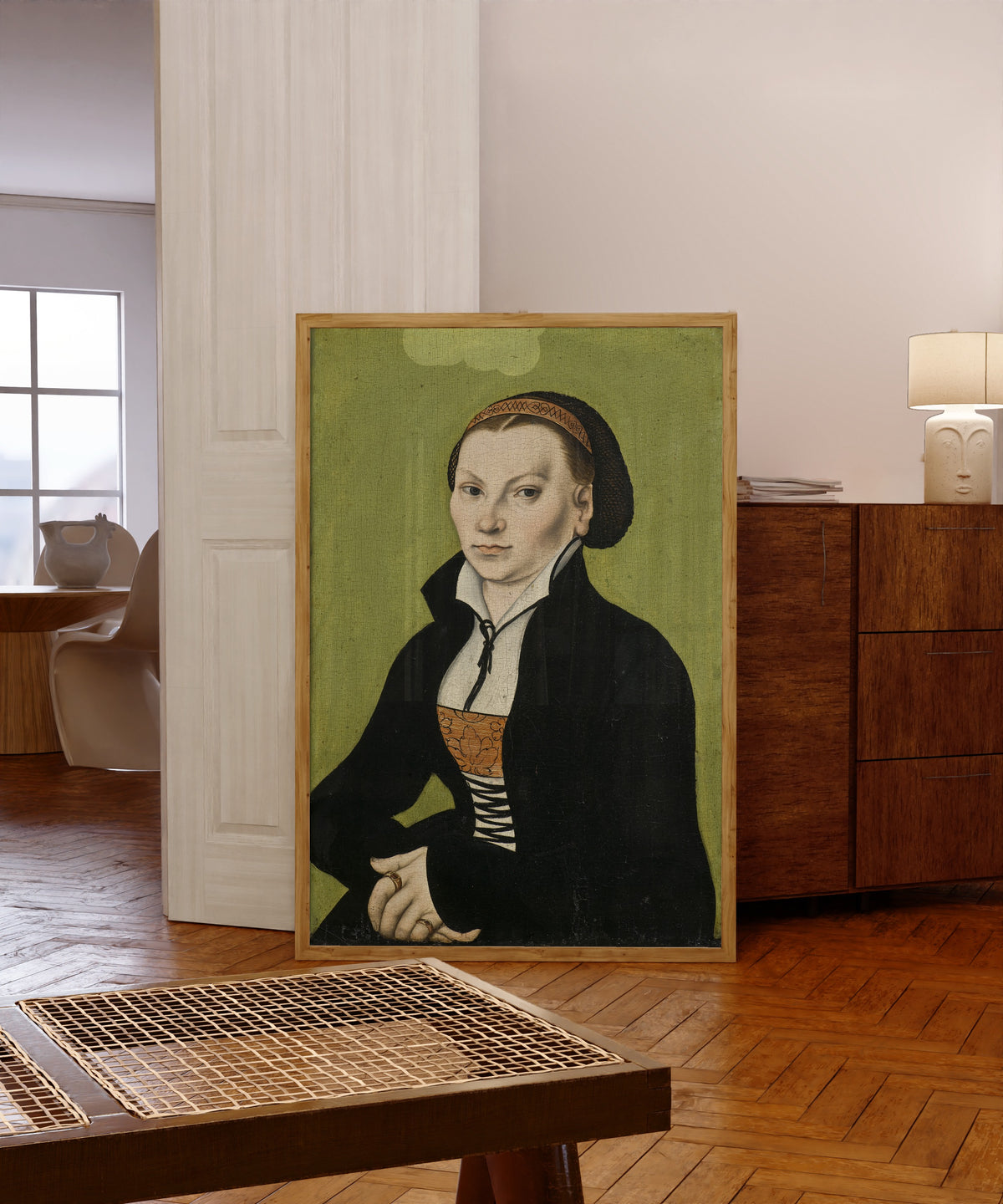 Framed art print of Katharina von Bora, Wife of Martin Luther by Lucas Cranach the Elder, in a light wood frame leaning in a warm room with a parquet floor