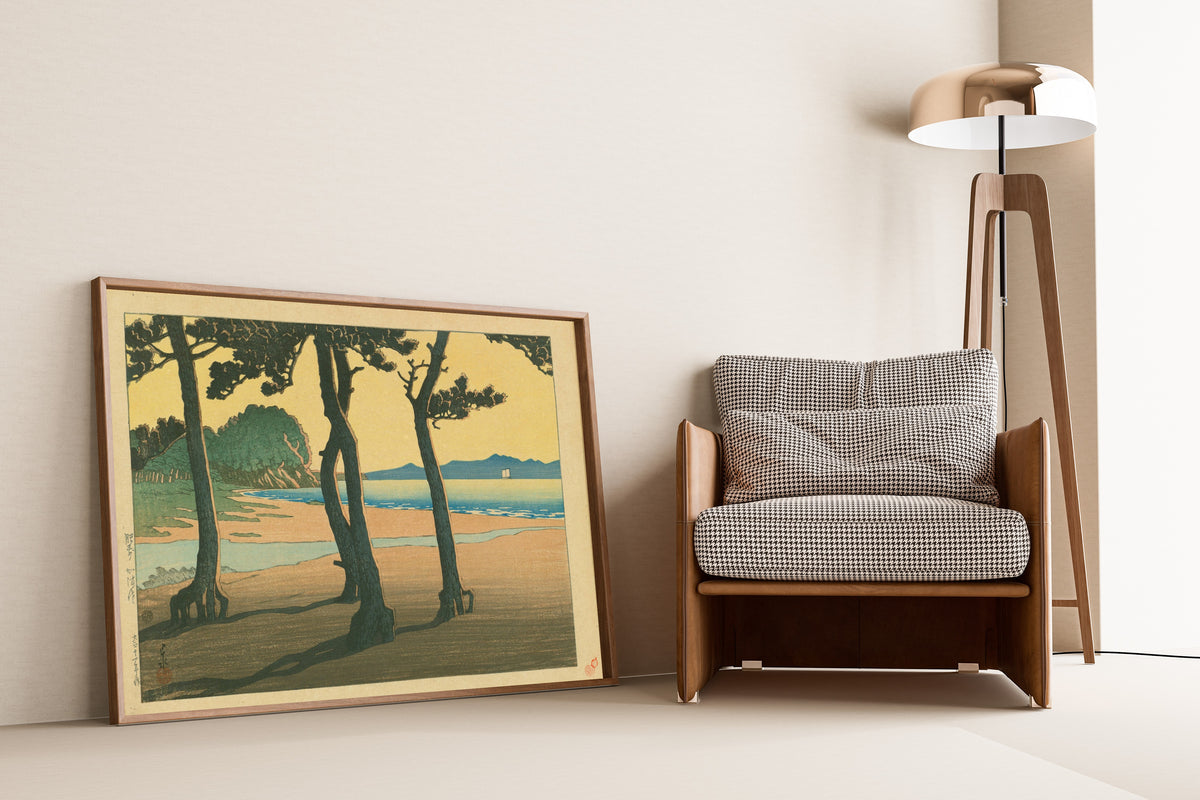 Framed art print of Kazusa Beach in Hizen Province by Kawase Hasui, leaning against a wall beside an armchair and a floor lamp
