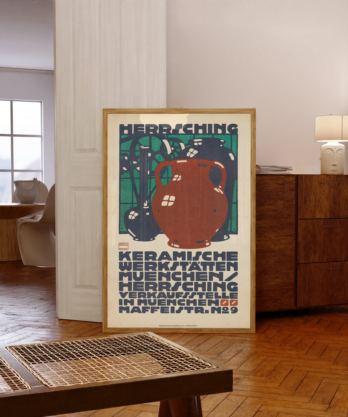 Framed art print of Keramische Werkstätten München: Herrsching by Ludwig Hohlwein, in a light wood frame leaning in a warm room with a parquet floor