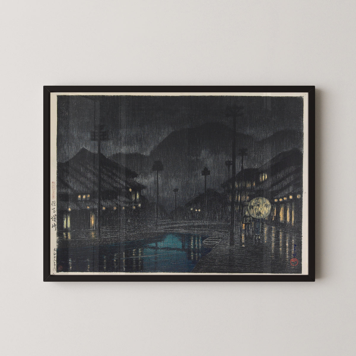 Framed art print of Kinosaki in Tajima Province by Kawase Hasui, in a black frame on a pale wall