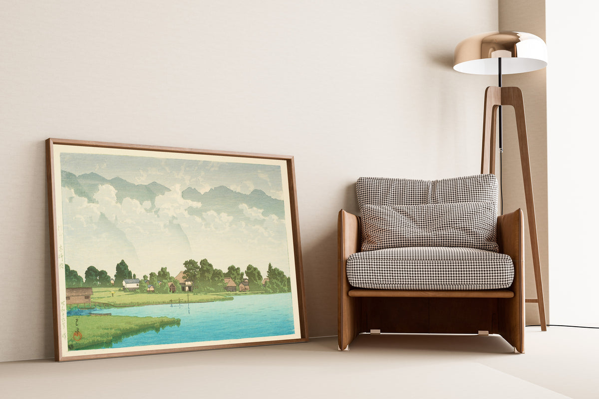 Framed art print of Kizaki Lake in Shinshu by Kawase Hasui, leaning against a wall beside an armchair and a floor lamp