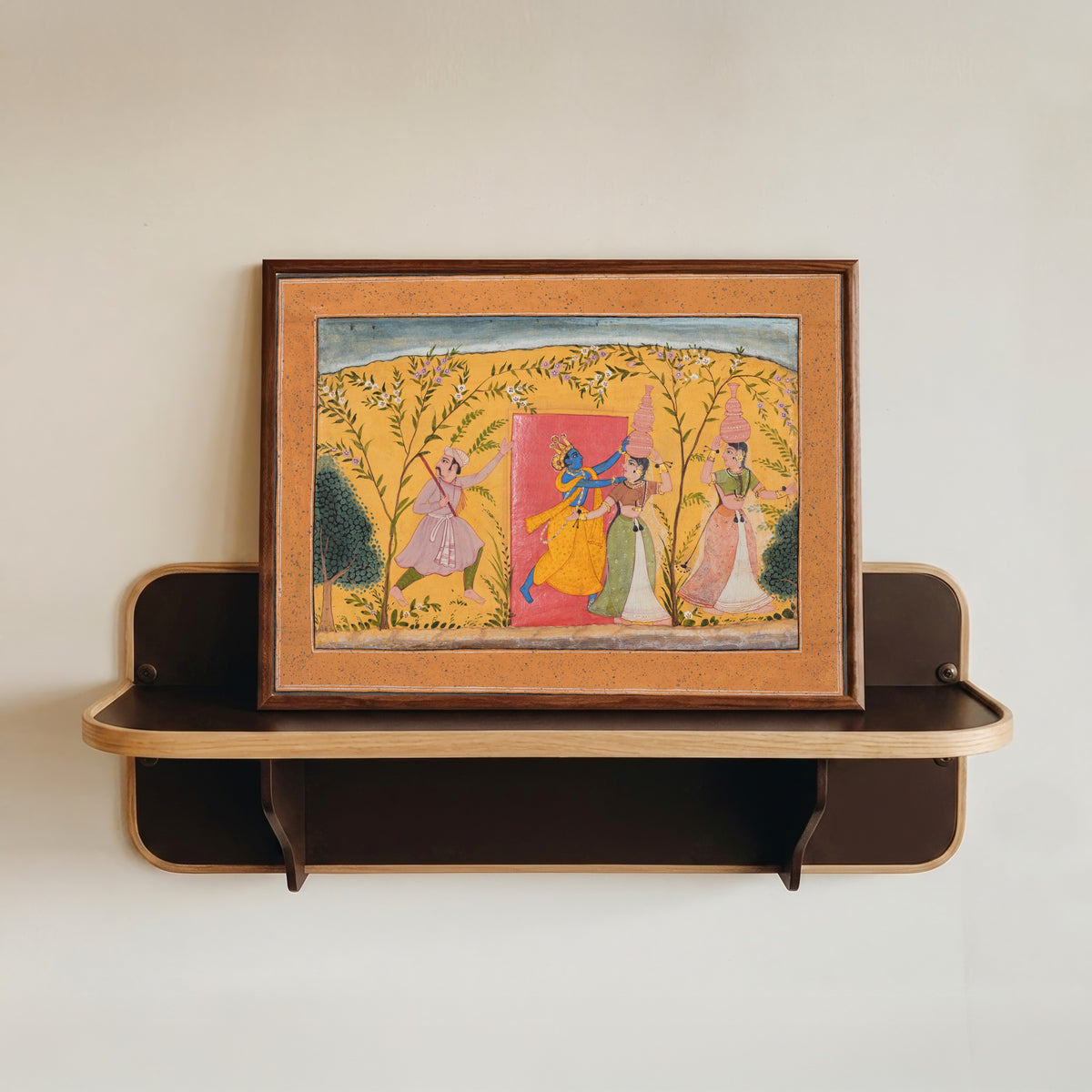 Framed art print of Krishna Exacts a Toll from the Milkmaids by Bikaner school, in a dark wood frame resting on a wall shelf