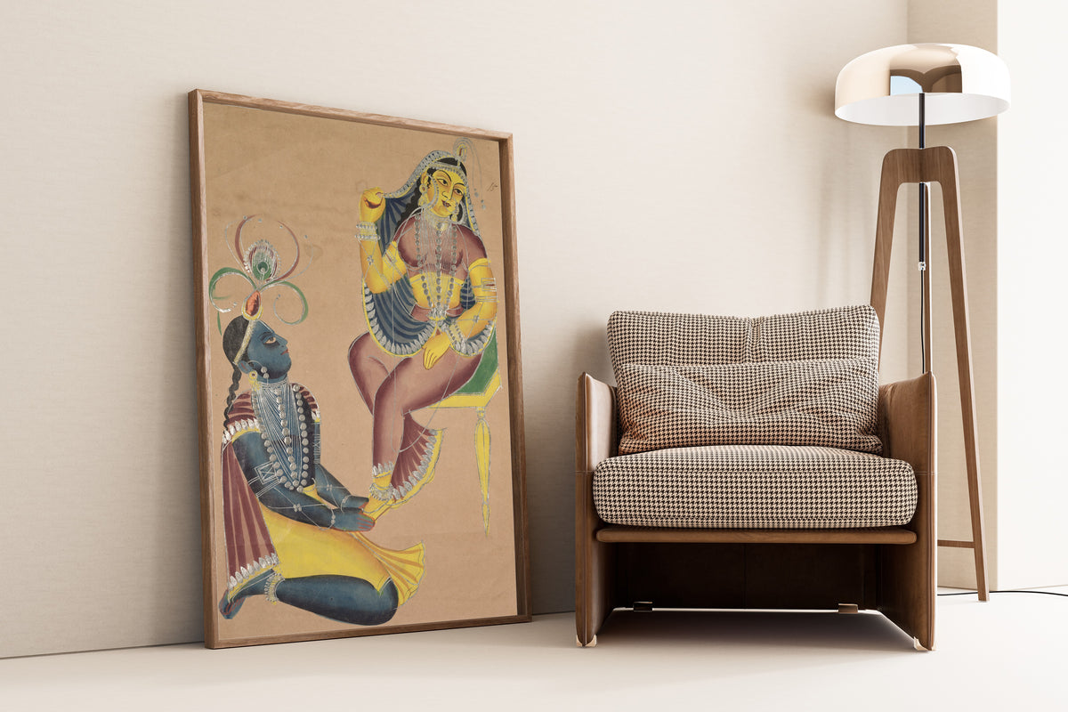 Framed art print of Krishna Stroking Radha's Feet by Kalighat painter, leaning against a wall beside an armchair and a floor lamp