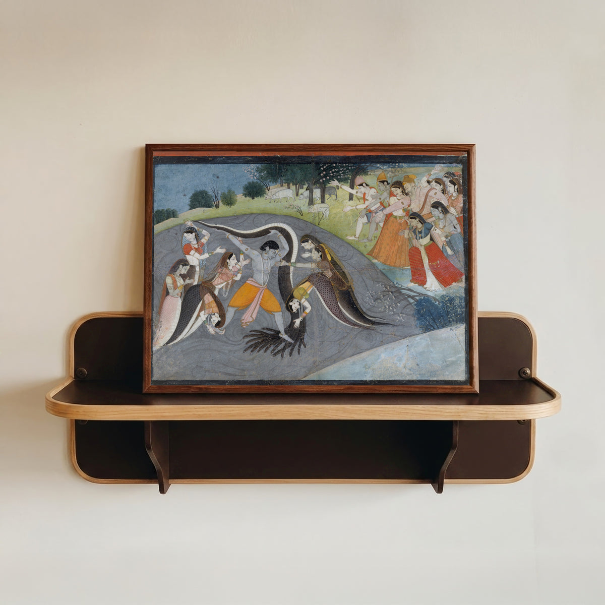Framed art print of Krishna Subduing Kaliya, the Snake Demon: Folio from a Bhagavata Purana… by Garhwal school, in a dark wood frame resting on a wall shelf