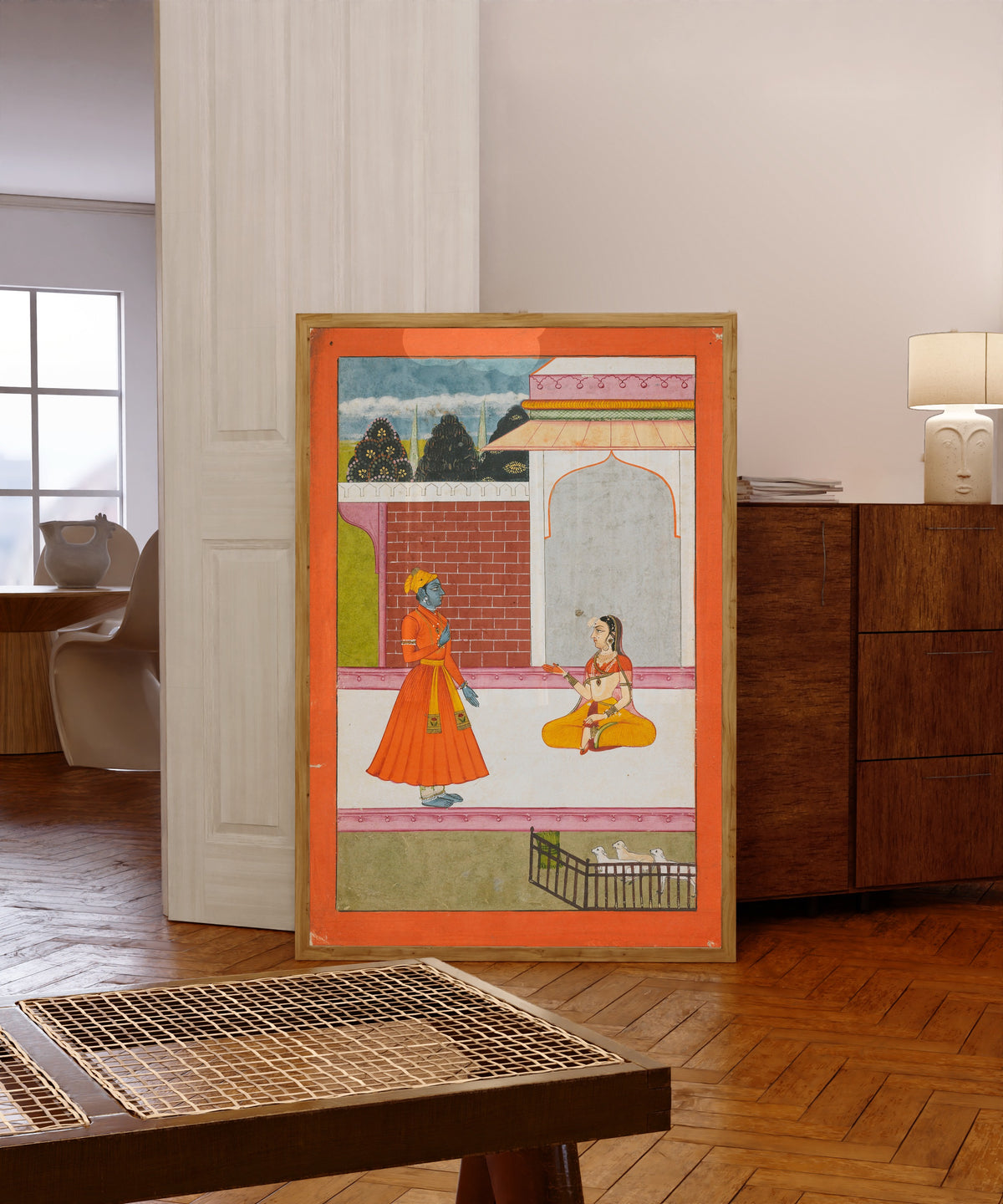 Framed art print of Krishna and Radha by Bikaner school, in a light wood frame leaning in a warm room with a parquet floor