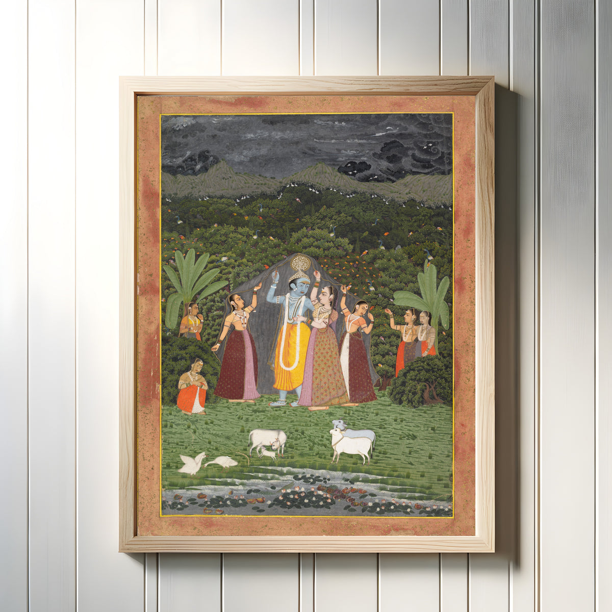 Framed art print of Krishna and the Gopis Take Shelter from the Rain by Jaipur school, in a light wood frame on a white panelled wall