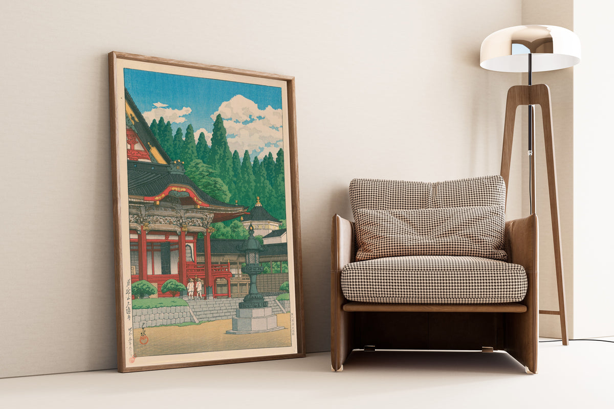 Framed art print of Kuonji Temple at Mount Minobu by Kawase Hasui, leaning against a wall beside an armchair and a floor lamp