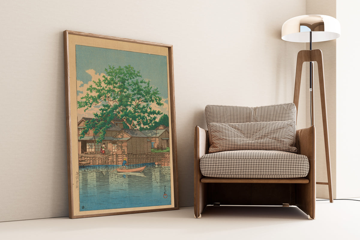 Framed art print of Kuri Ferry, Funabori by Kawase Hasui, leaning against a wall beside an armchair and a floor lamp