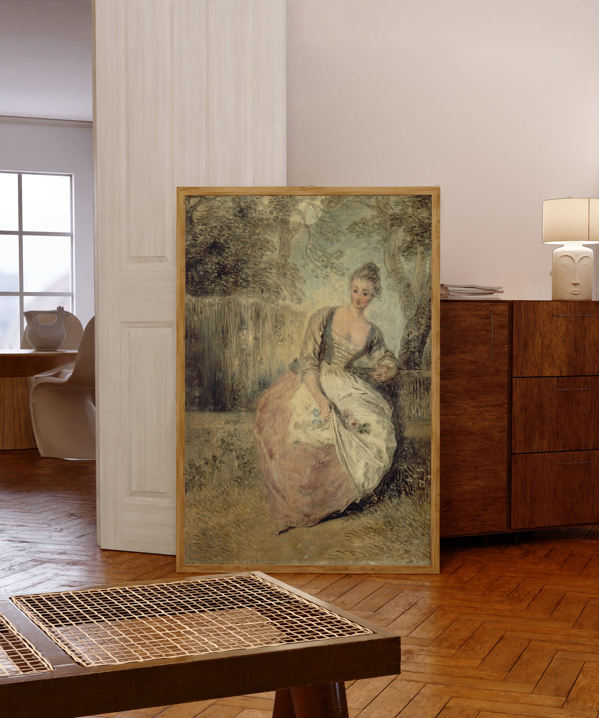Framed art print of L'Amante inquiète by Jean-Antoine Watteau, in a light wood frame leaning in a warm room with a parquet floor