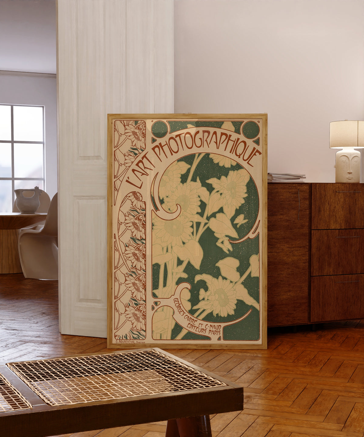 Framed art print of L’Art Photographique, no. 10 (cover) by Alphonse Mucha, in a light wood frame leaning in a warm room with a parquet floor
