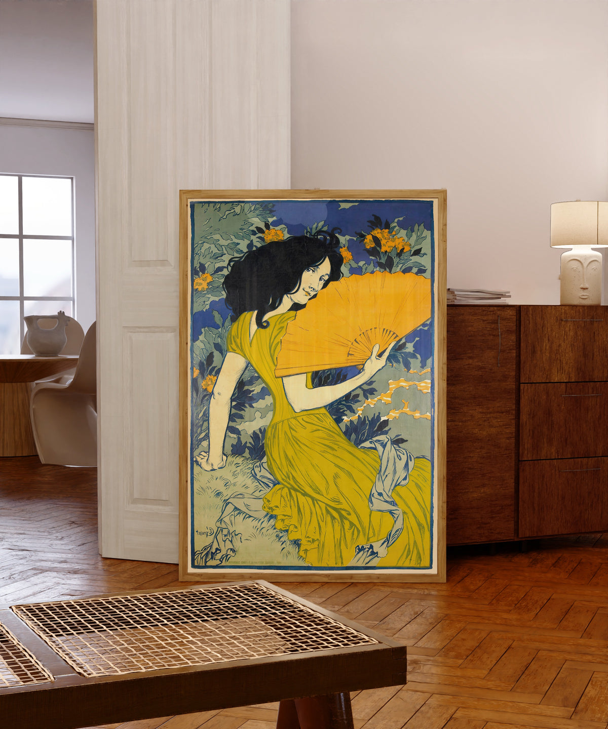 Framed art print of L'Éventail by Eugène Grasset, in a light wood frame leaning in a warm room with a parquet floor