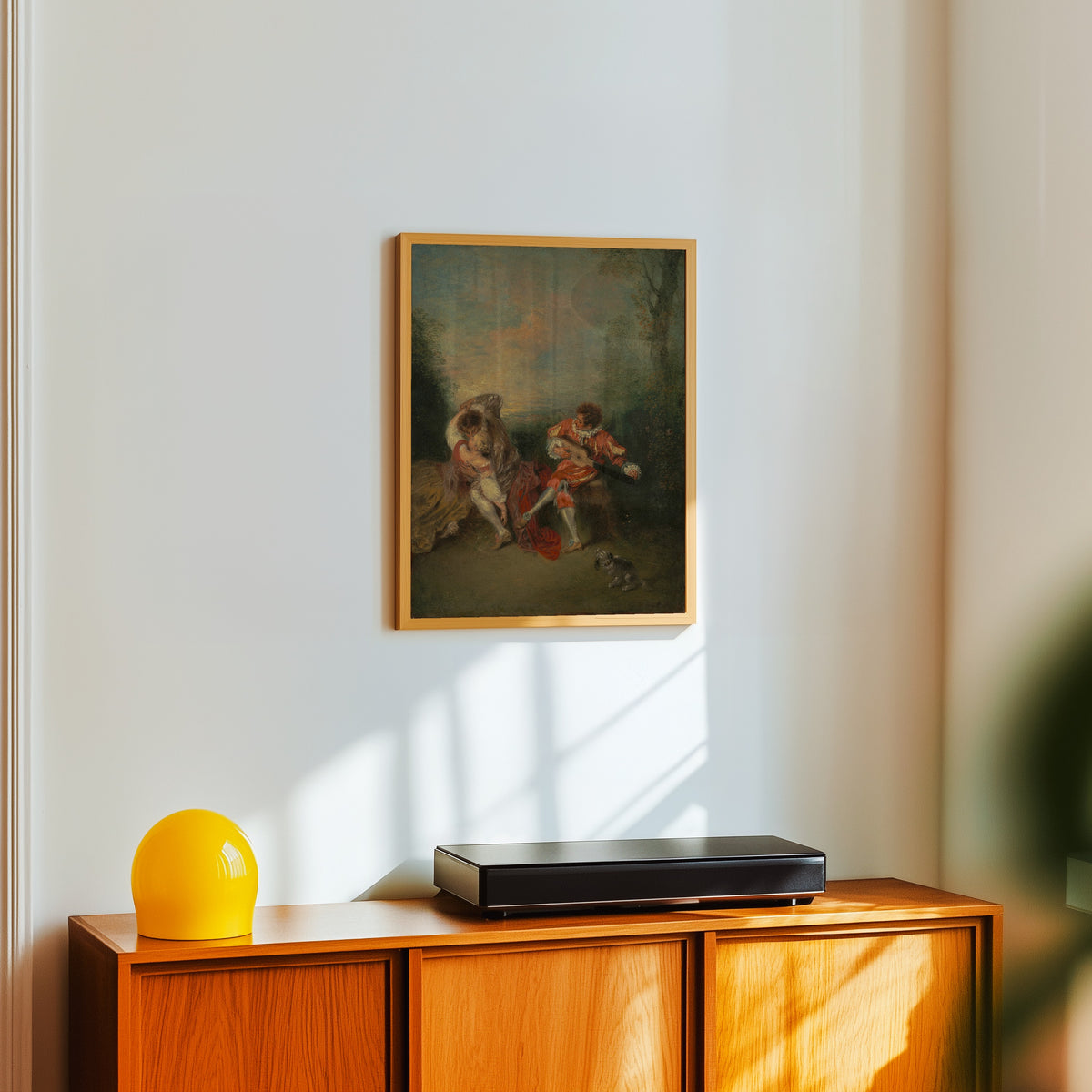 Framed art print of La Surprise by Jean-Antoine Watteau, in a light wood frame on a white wall above an orange sideboard
