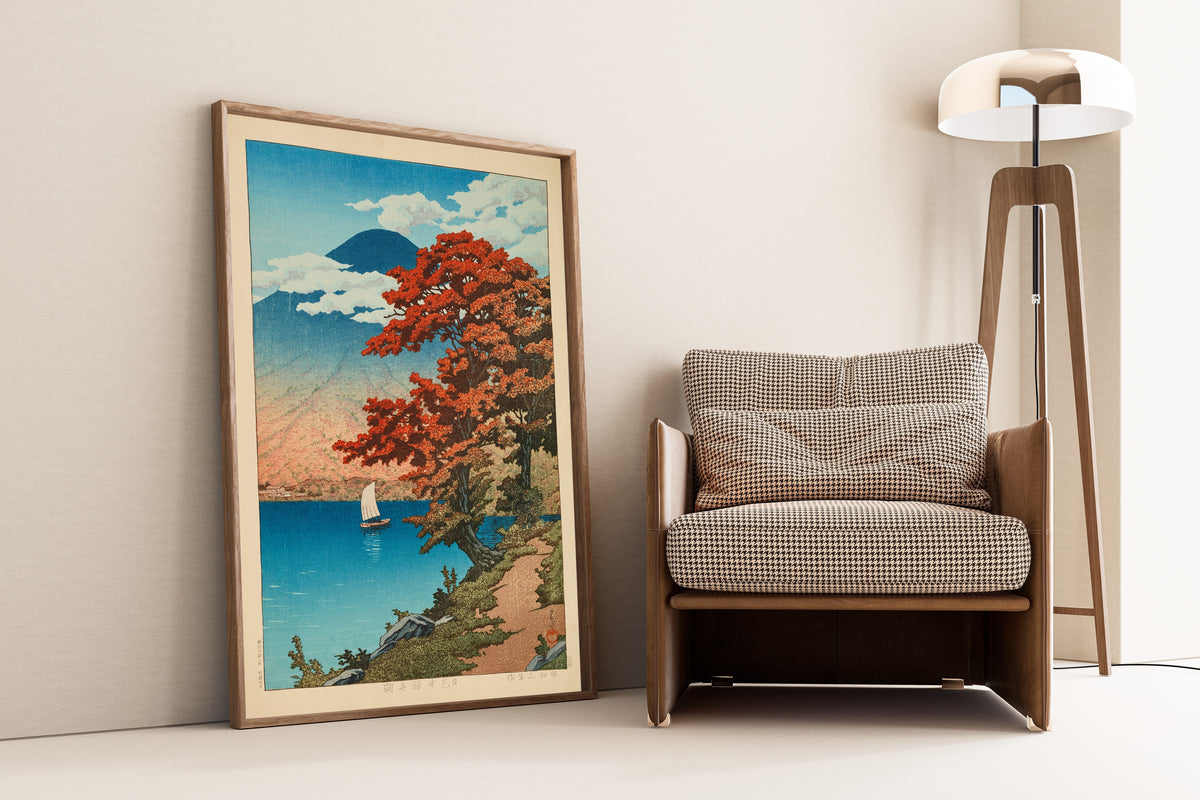 Framed art print of Lake Chuzenji at Nikko by Kawase Hasui, leaning against a wall beside an armchair and a floor lamp