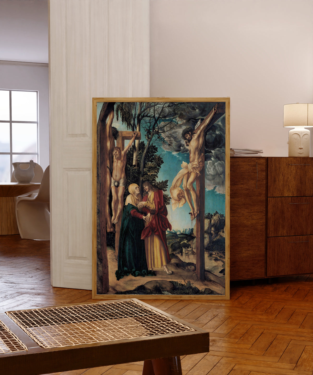 Framed art print of Lamentation under the Cross by Lucas Cranach the Elder, in a light wood frame leaning in a warm room with a parquet floor