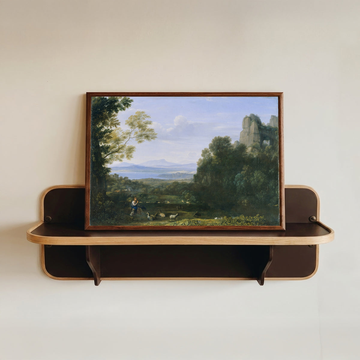 Framed art print of Landscape with Apollo and Mercury by Claude Lorrain, in a dark wood frame resting on a wall shelf