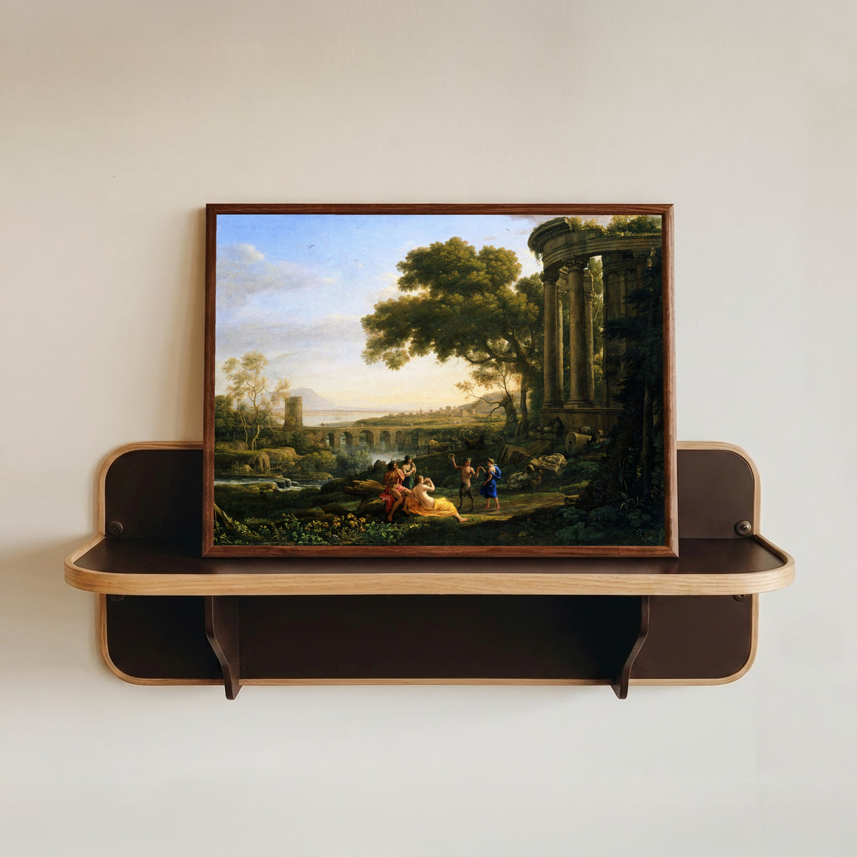 Framed art print of Landscape with Nymph and Satyr Dancing by Claude Lorrain, in a dark wood frame resting on a wall shelf