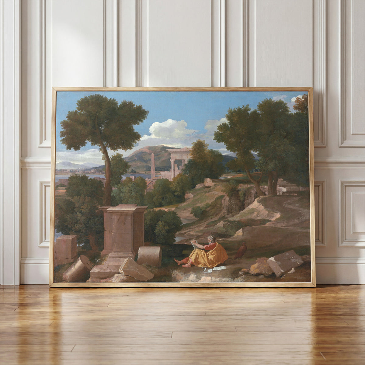 Framed art print of Landscape with Saint John on Patmos by Nicolas Poussin, in a light wood frame leaning against a panelled white wall