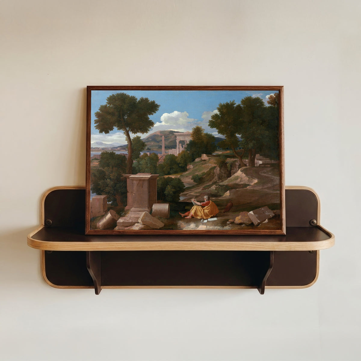 Framed art print of Landscape with Saint John on Patmos by Nicolas Poussin, in a dark wood frame resting on a wall shelf