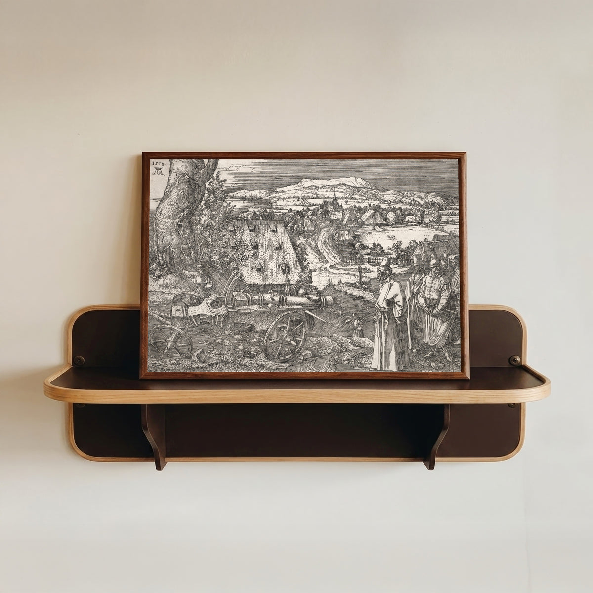 Framed art print of Landscape with the Cannon by Albrecht Dürer, in a dark wood frame resting on a wall shelf
